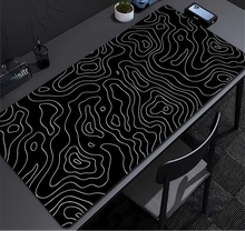 Black and white topographic desk mat on a desk with office items.